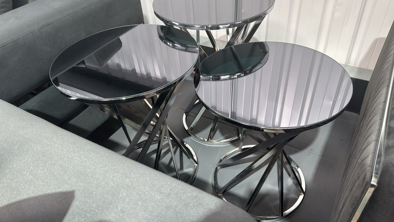 Three round tables with black glossy tops and twisted silver metal bases between gray sofas.