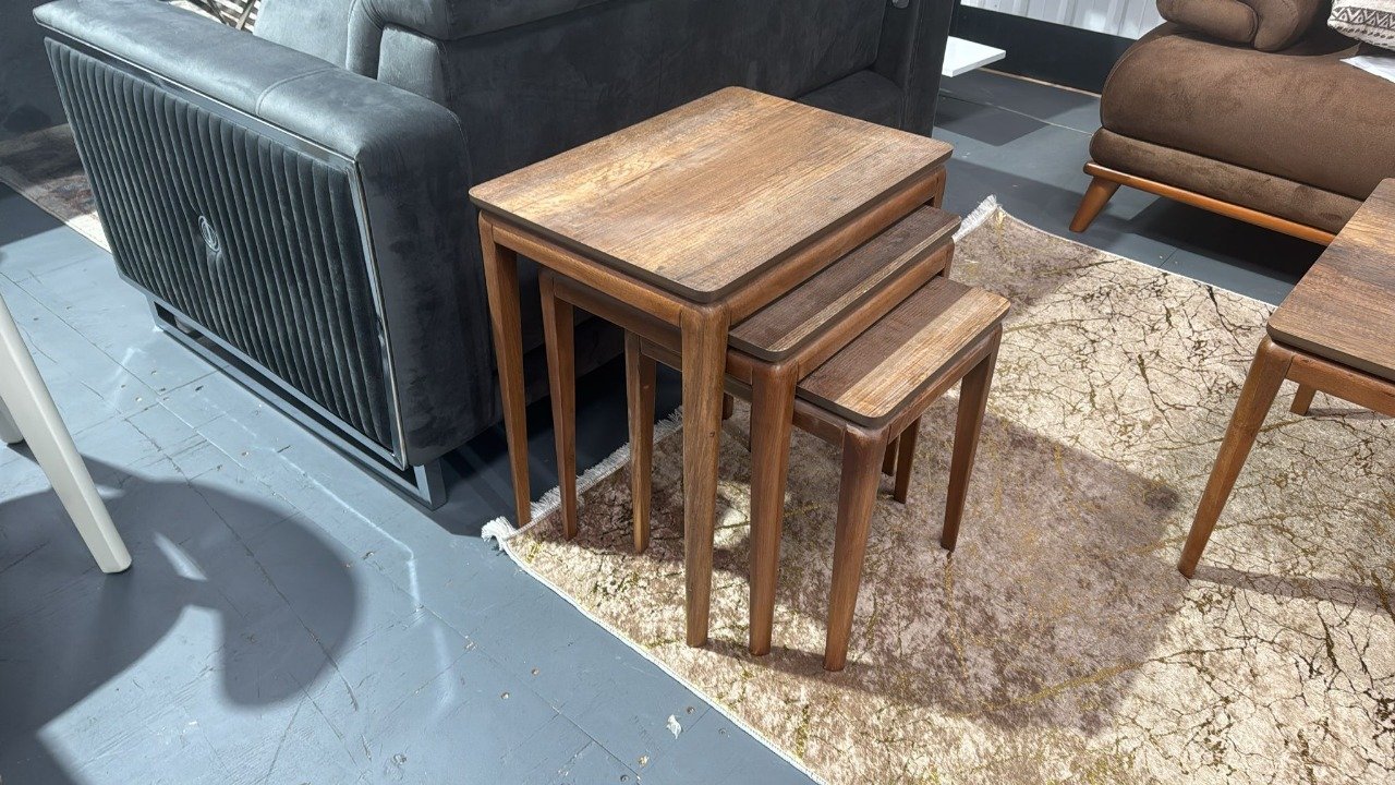 Set of three wooden nesting Edgewood Coffee Tables on a patterned rug beside a dark gray sofa.