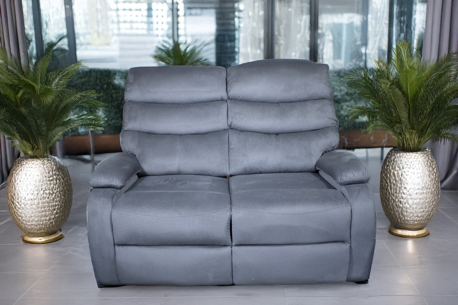 Gray reclining sofa between two potted plants in a modern living room.