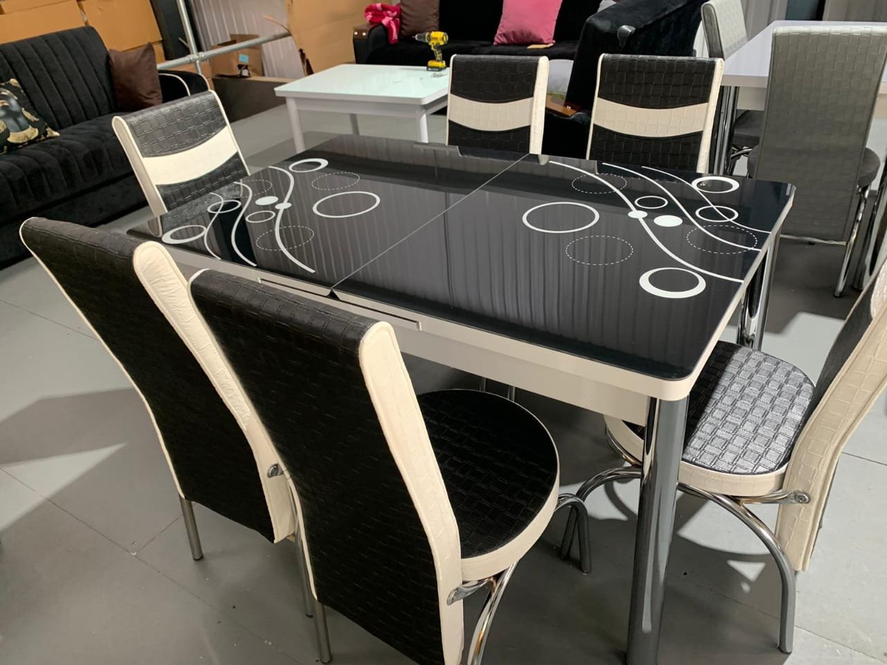 OptraGlass Extendable Table with a black glossy surface and white circular patterns, surrounded by six black and white chairs.