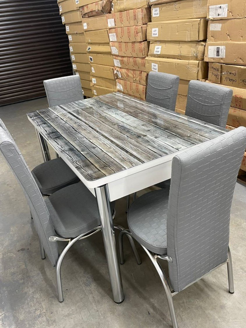 VerraStretch Dining Table with a rustic wooden top and gray upholstered chairs in a warehouse.