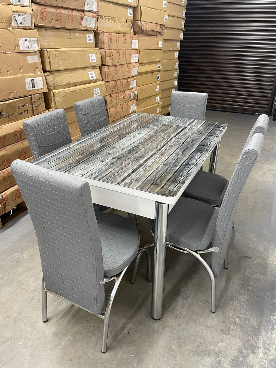 VerraStretch Dining Table with a rustic wooden top and gray upholstered chairs in a warehouse.