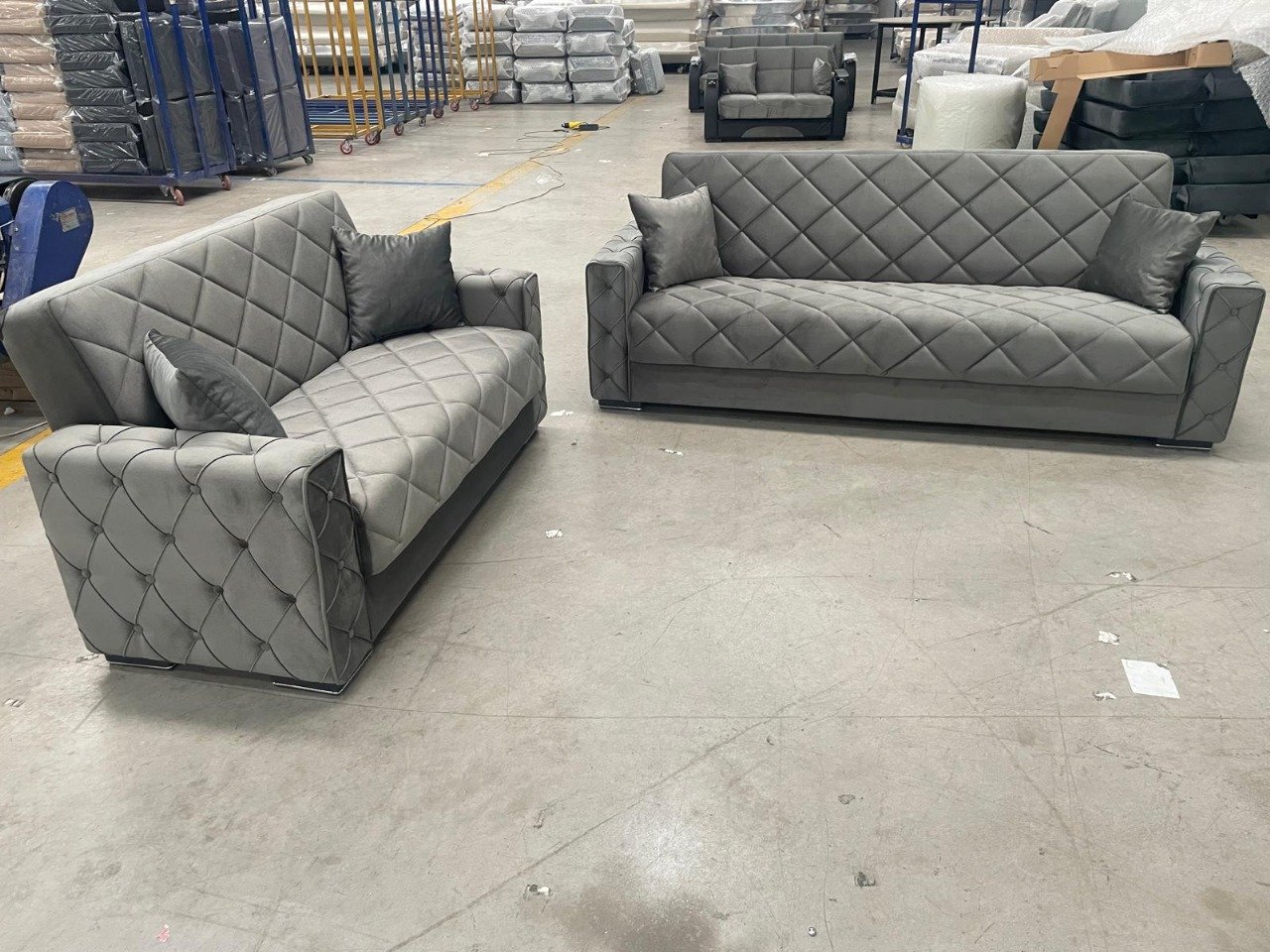 Two gray tufted sofas in a warehouse.